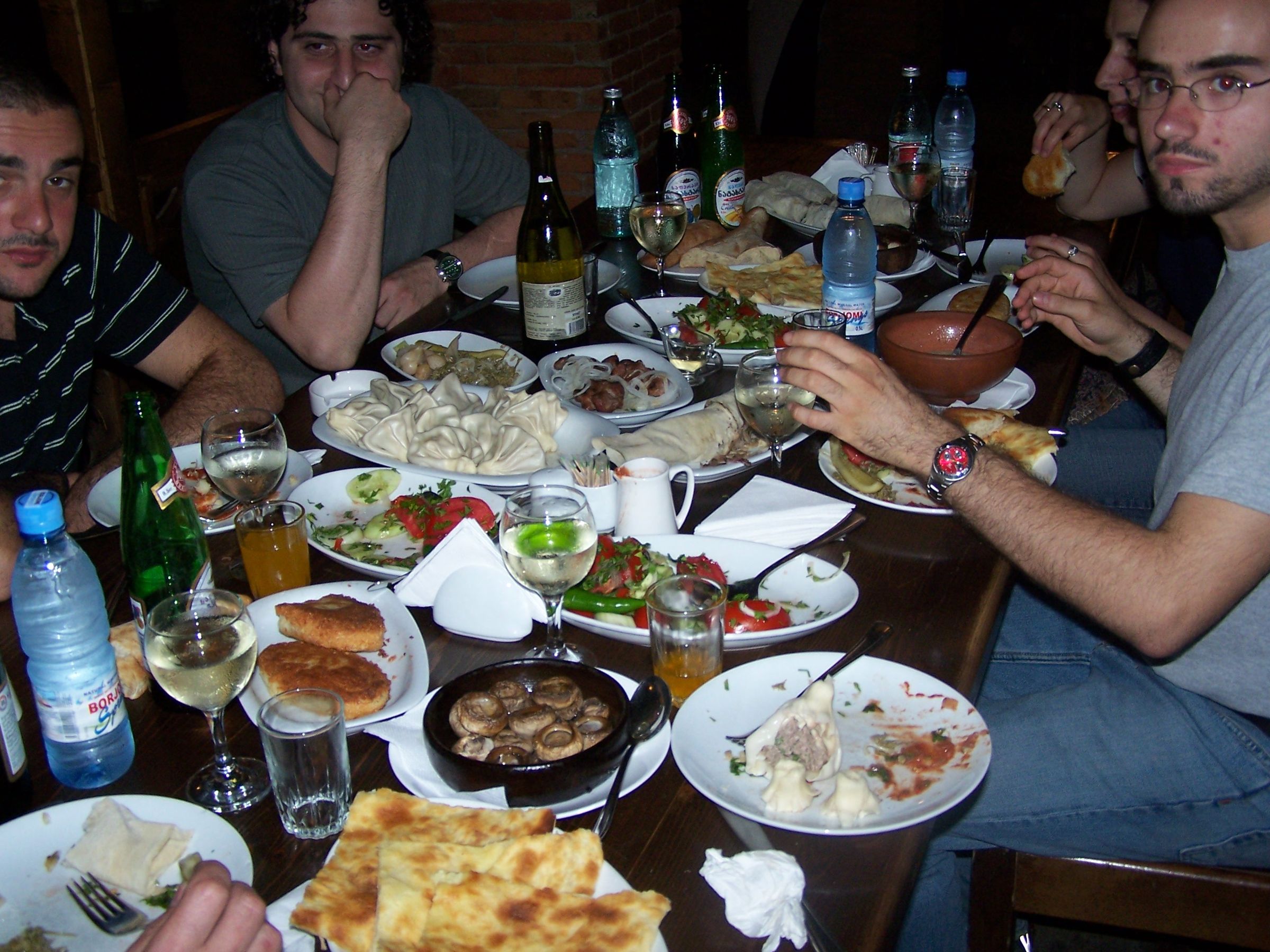 A Georgian supra table seen close: hands, bread, wine, the moment before a toast. No posed smiles.