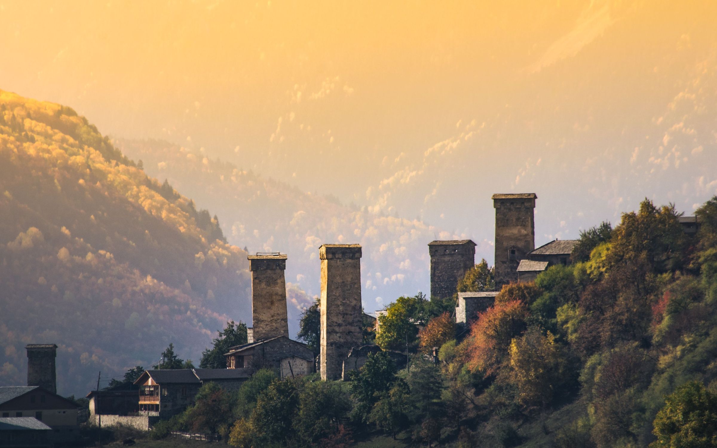 Svaneti towers at golden hour, a figure-scale roof against the range.